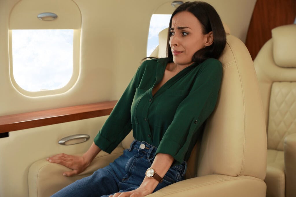 Woman needing hypnotherapy for fear of flying - looking very anxious sitting in seat in aeroplane